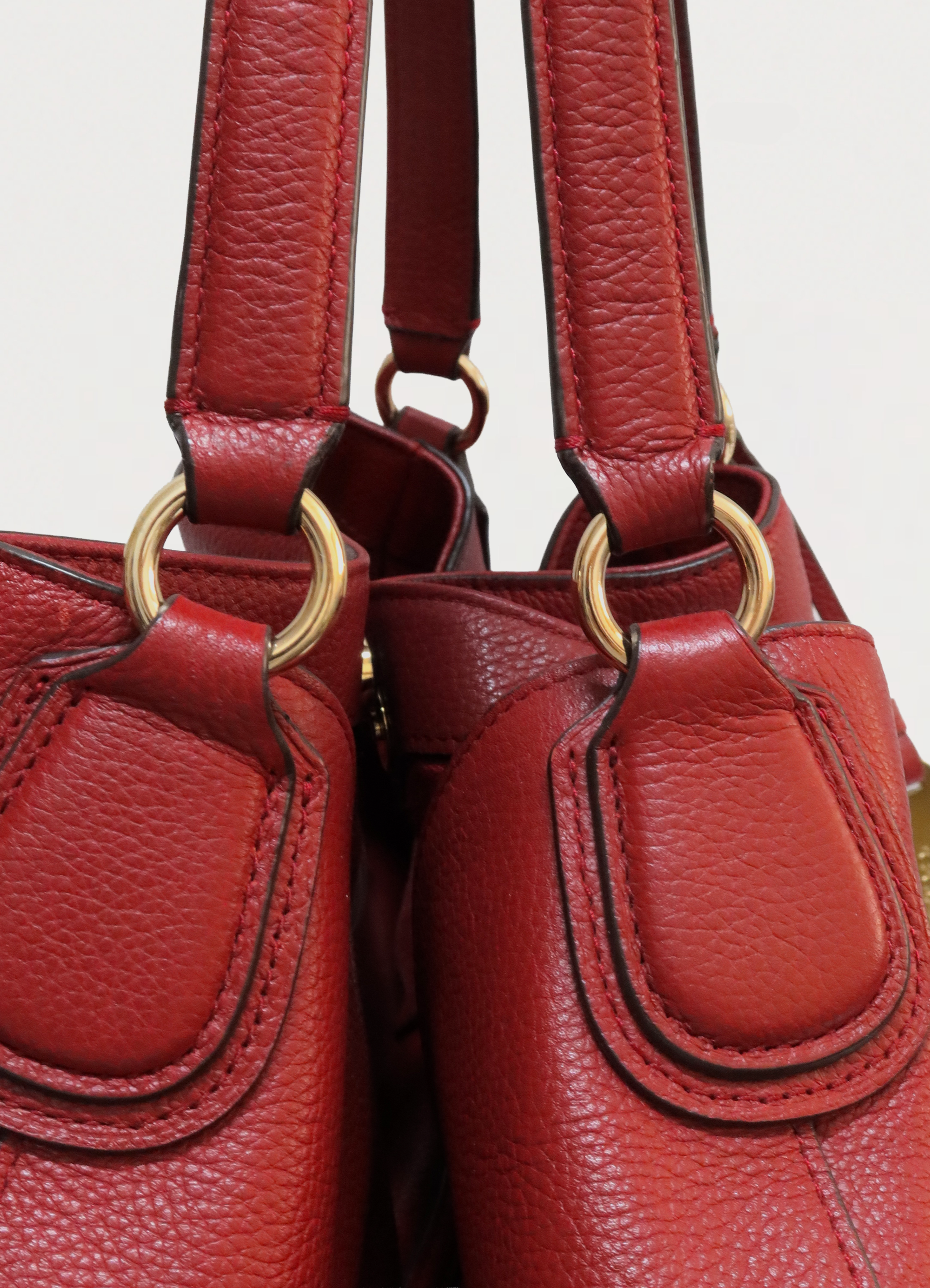 Detail of gold-tone metal rings and strap attachment on red Coach bag