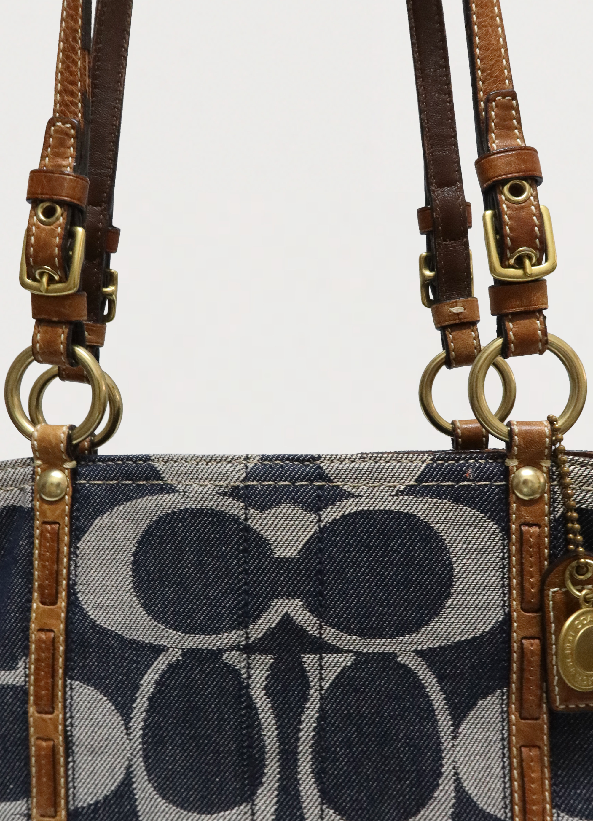 Close up of brass hardware and tan leather strap attachments on Coach denim bag