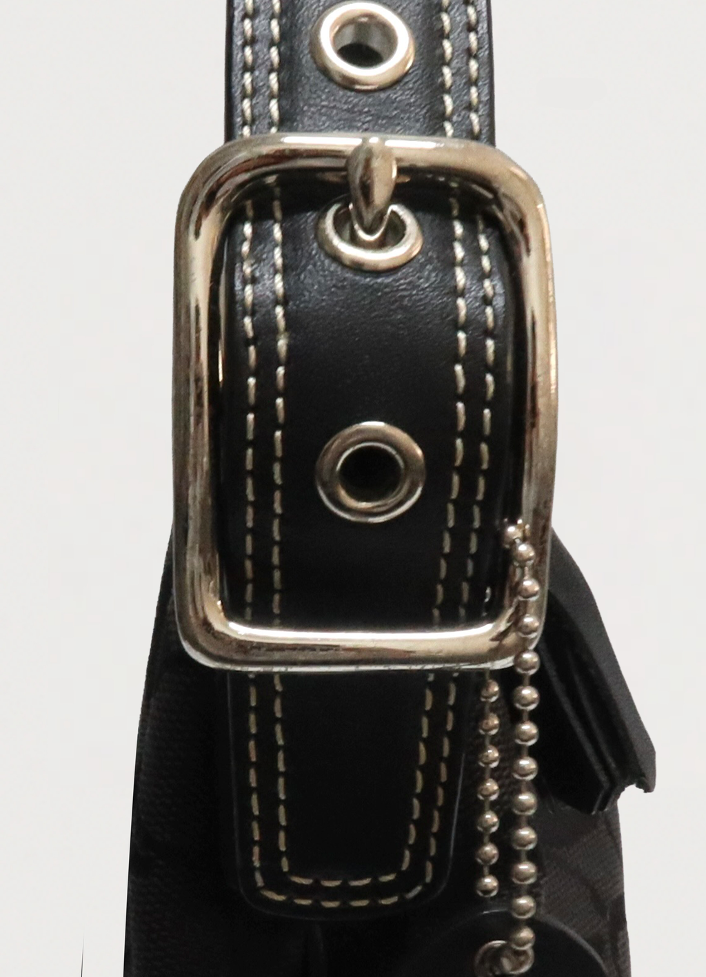 Macro detail of silver-tone buckle and grommets on Coach baguette strap
