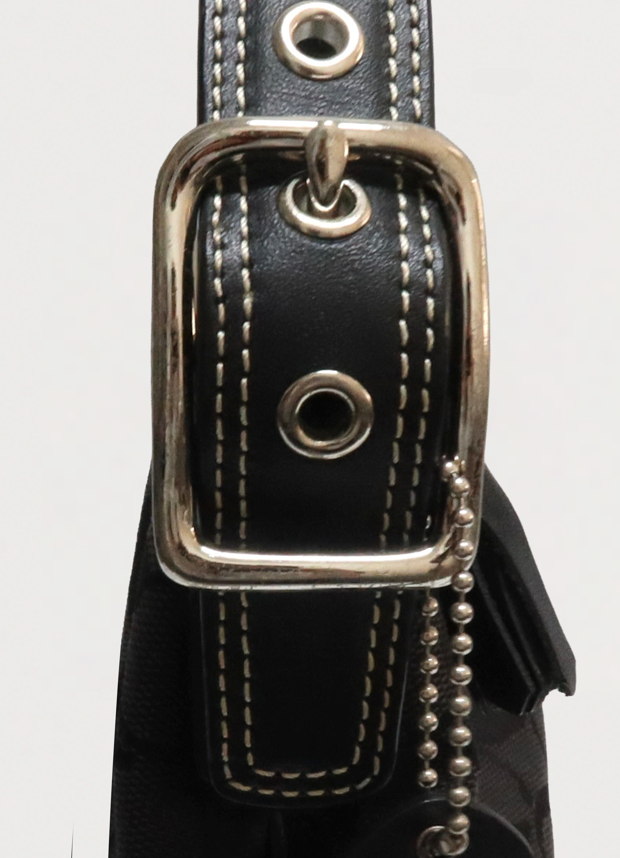 Macro detail of silver-tone buckle and grommets on Coach baguette strap