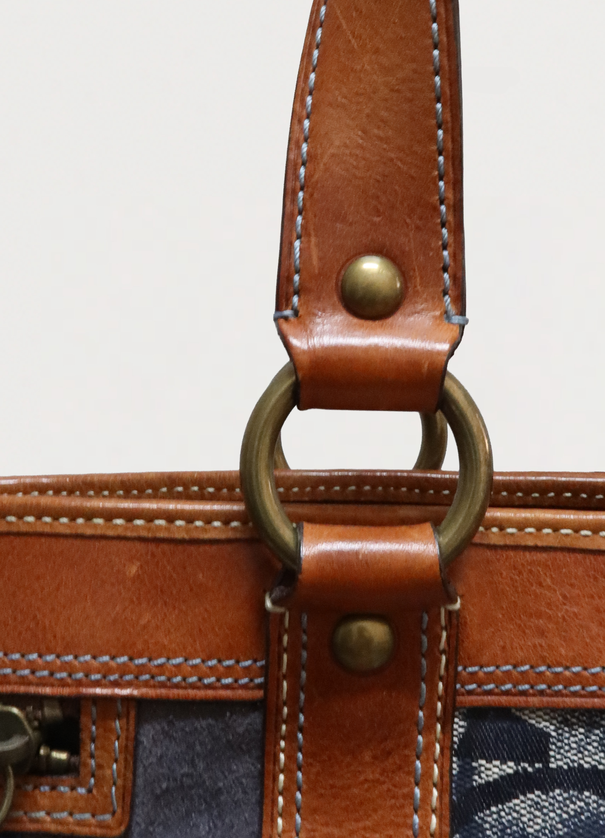 Detail of the tan leather shoulder strap and brass rivet hardware on Coach Legacy tote