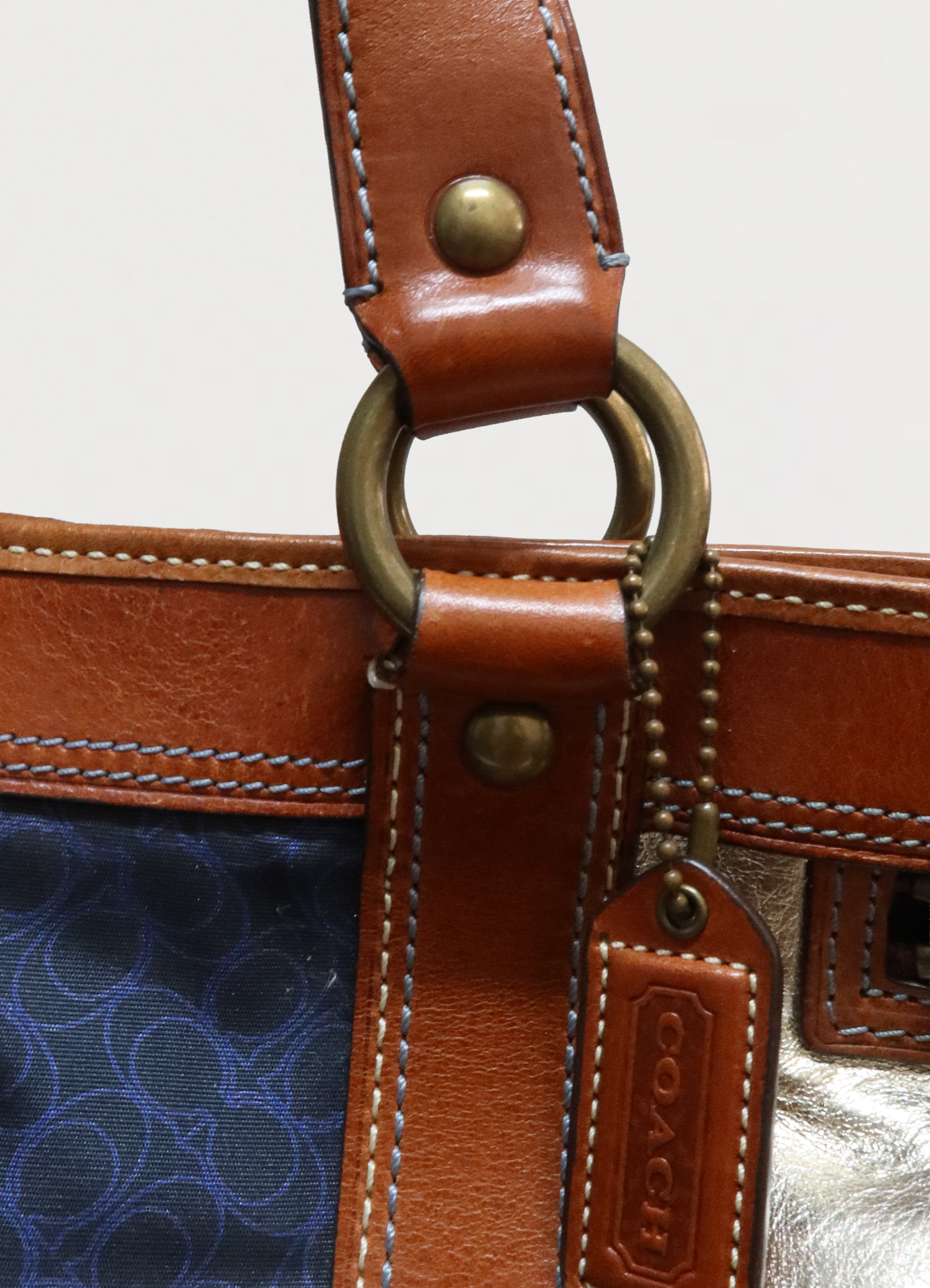 Detail of the tan leather shoulder strap and brass rivet hardware on Coach Legacy tote