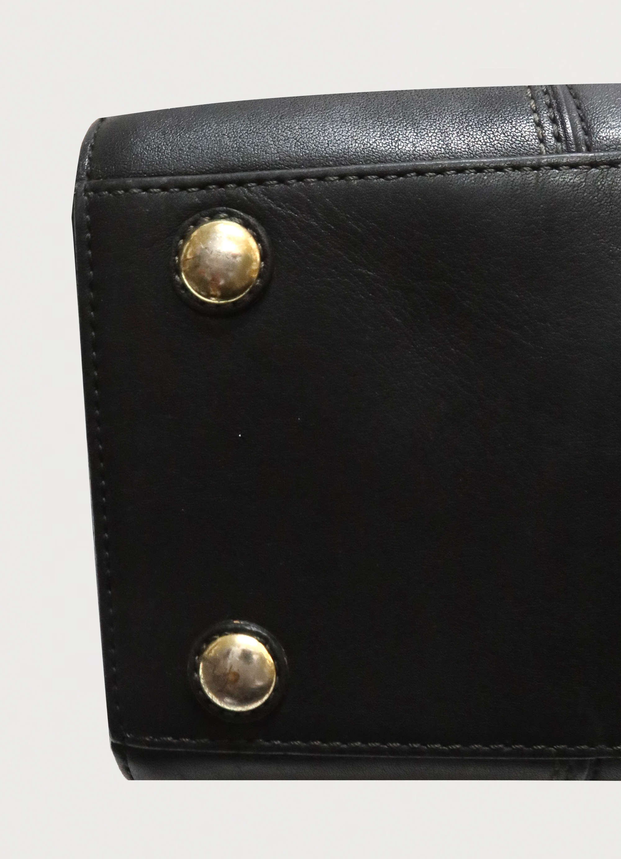 Detail shot of the polished brass feet on the base of the black Coach satchel