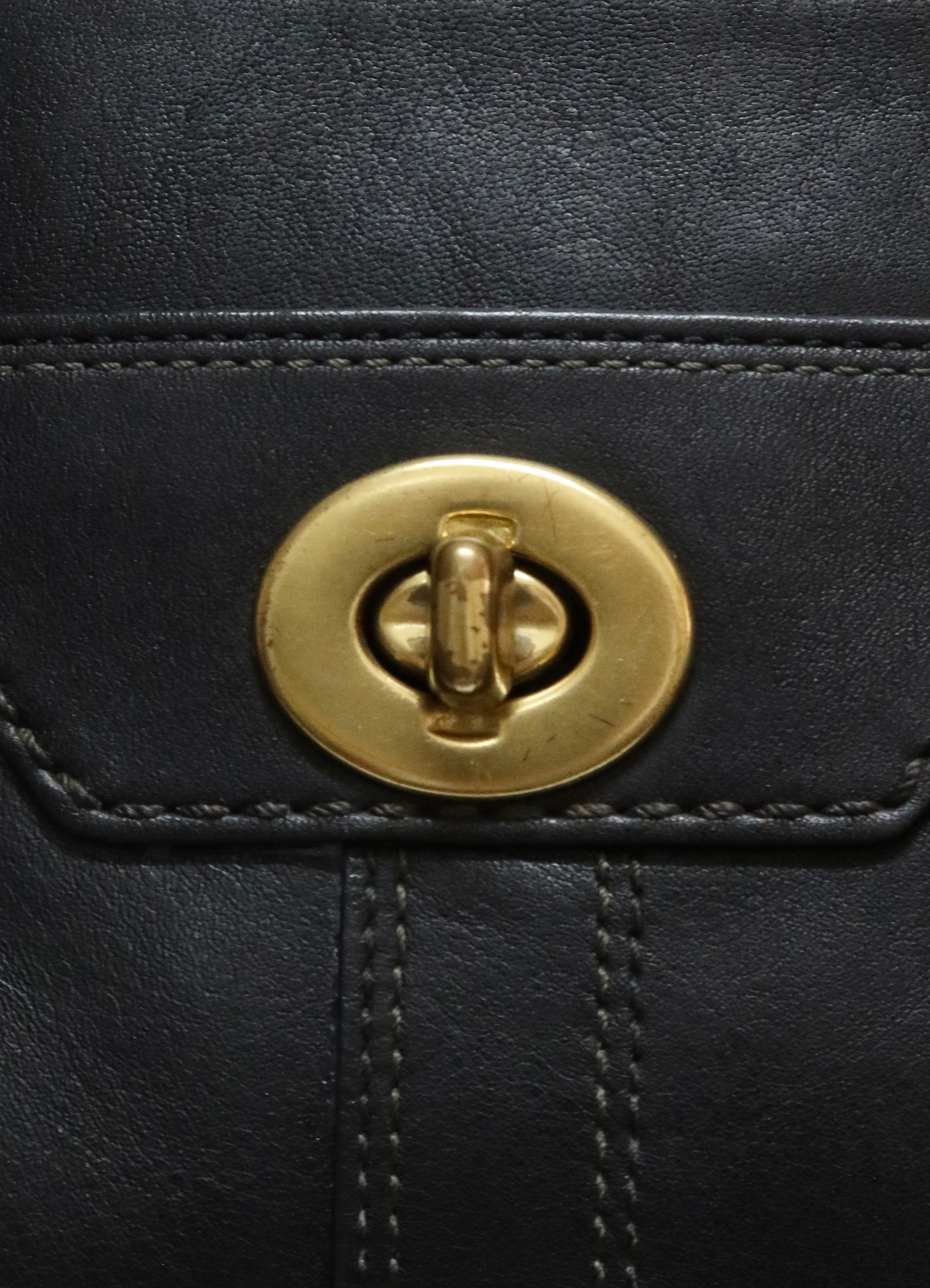 Close up of the signature brass turnlock closure on the front pocket of the Coach bag