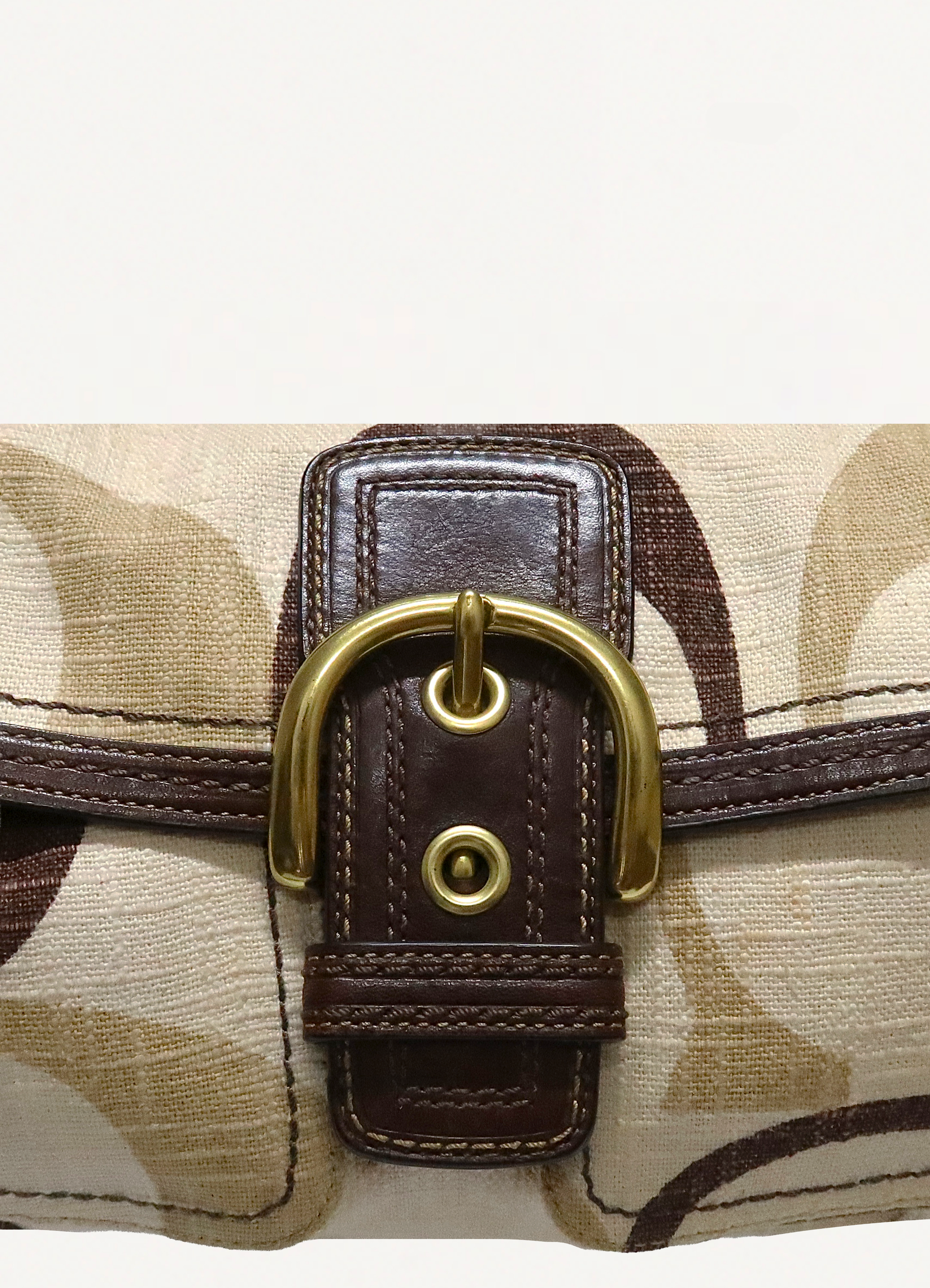 Close up of large brass buckle and mocha brown leather strap on Coach Soho flap