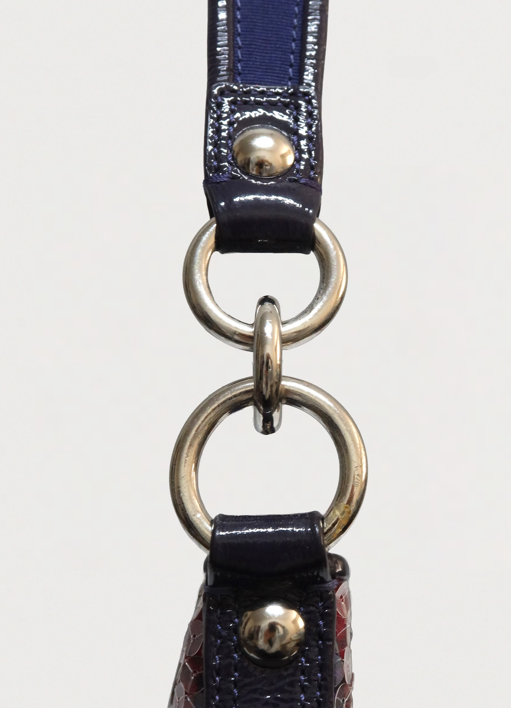 Close up of silver-tone hardware rings and purple patent leather strap attachment