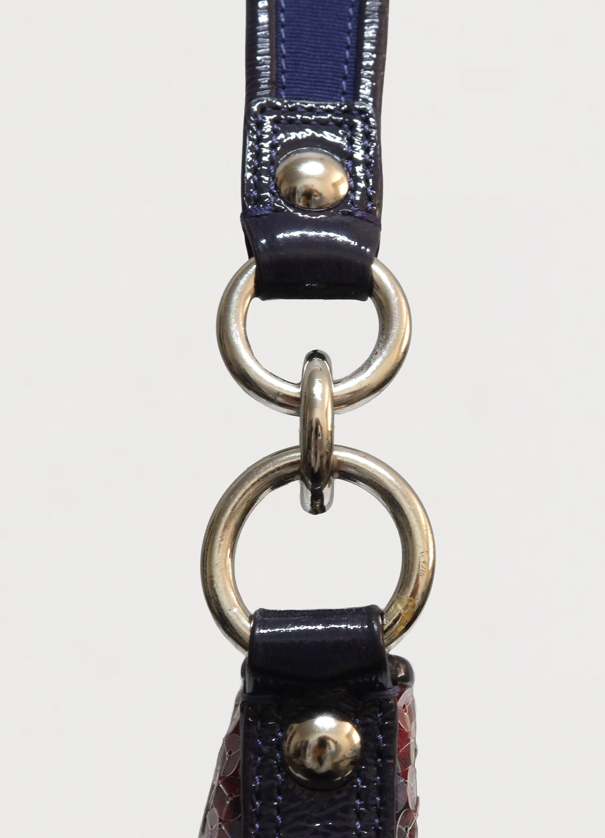 Close up of silver-tone hardware rings and purple patent leather strap attachment