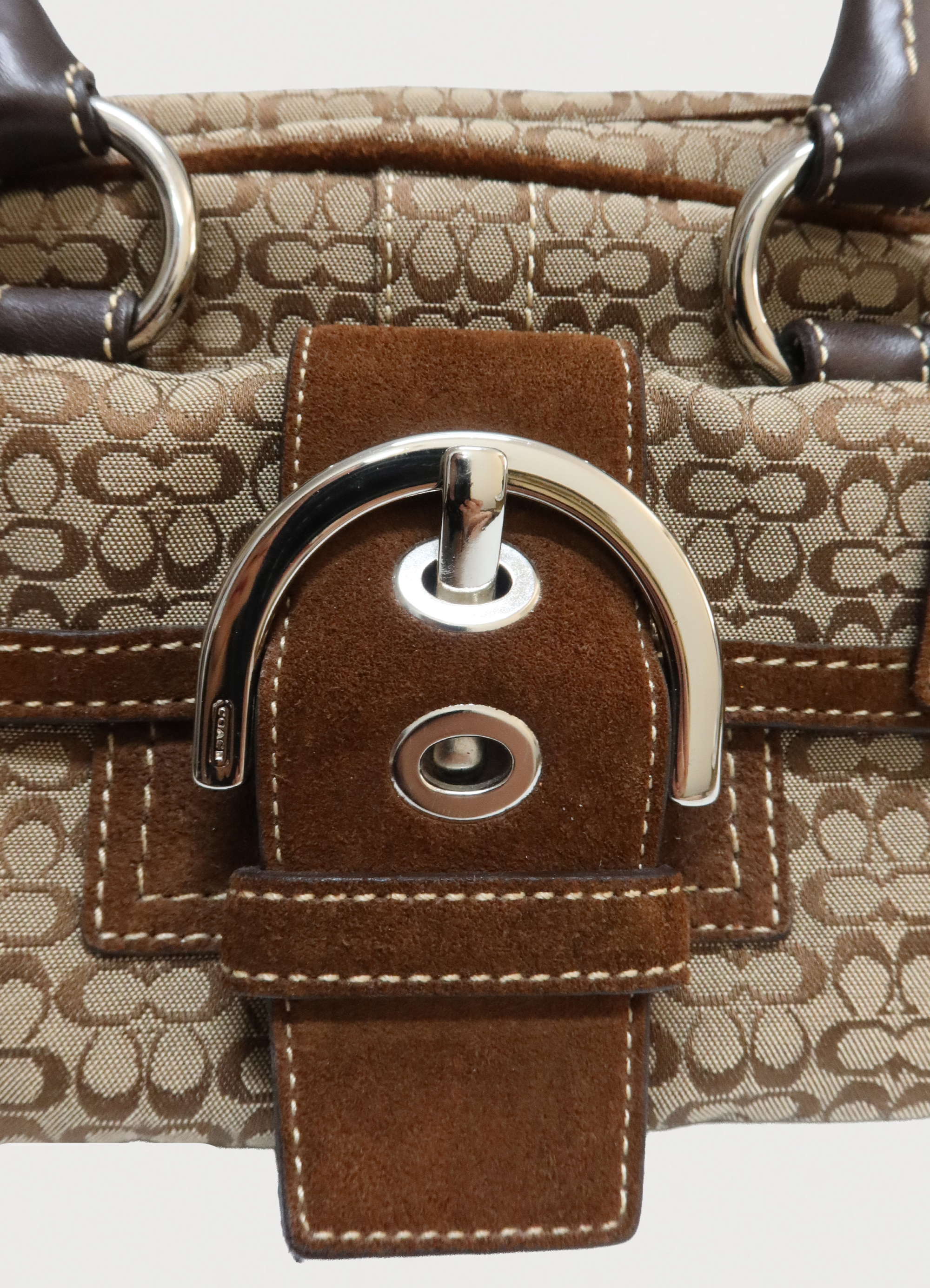 Macro detail of silver-tone buckle and brown suede texture on the front flap