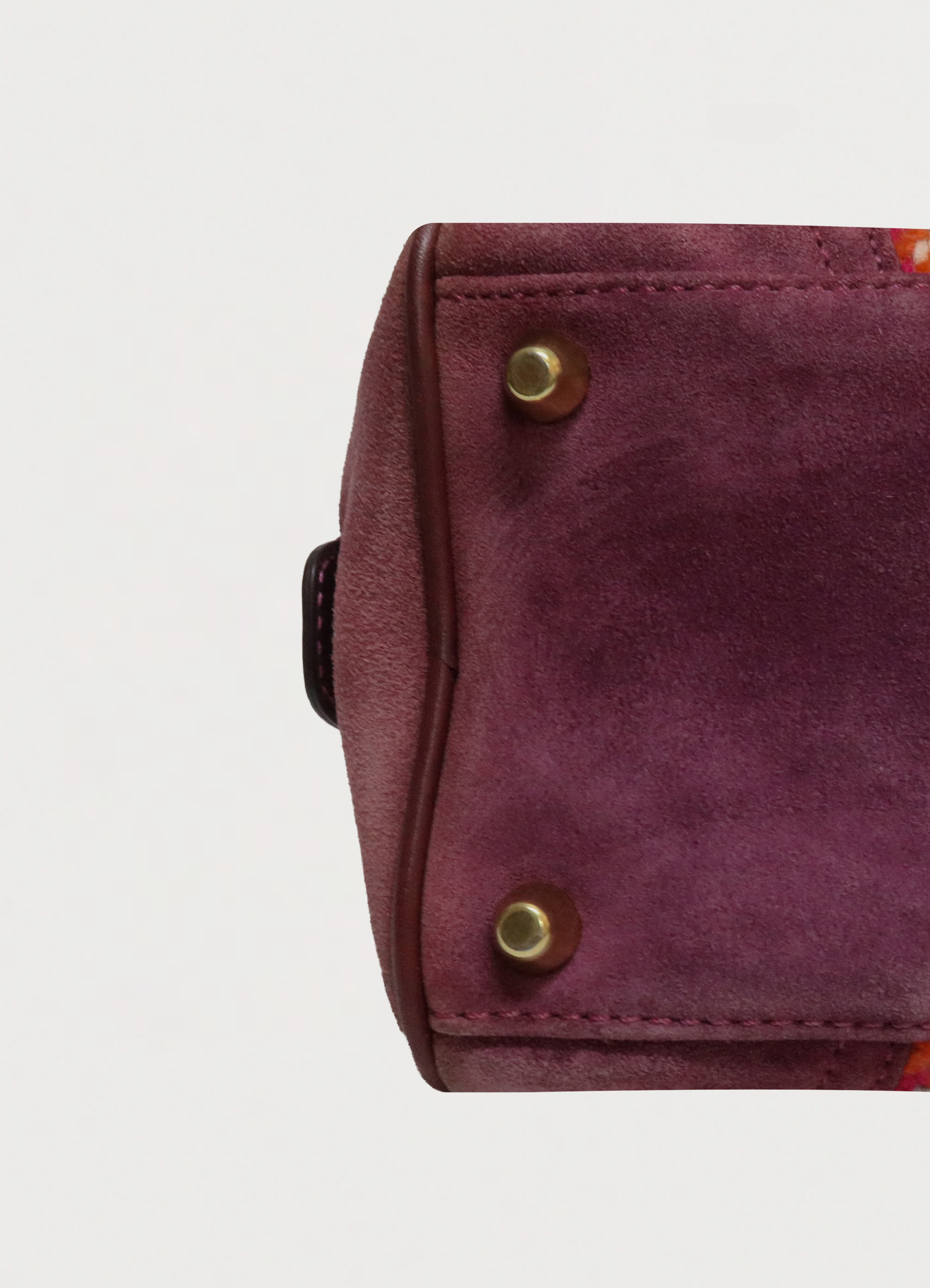 Close up of berry suede corner and brass protective foot on Coach satchel