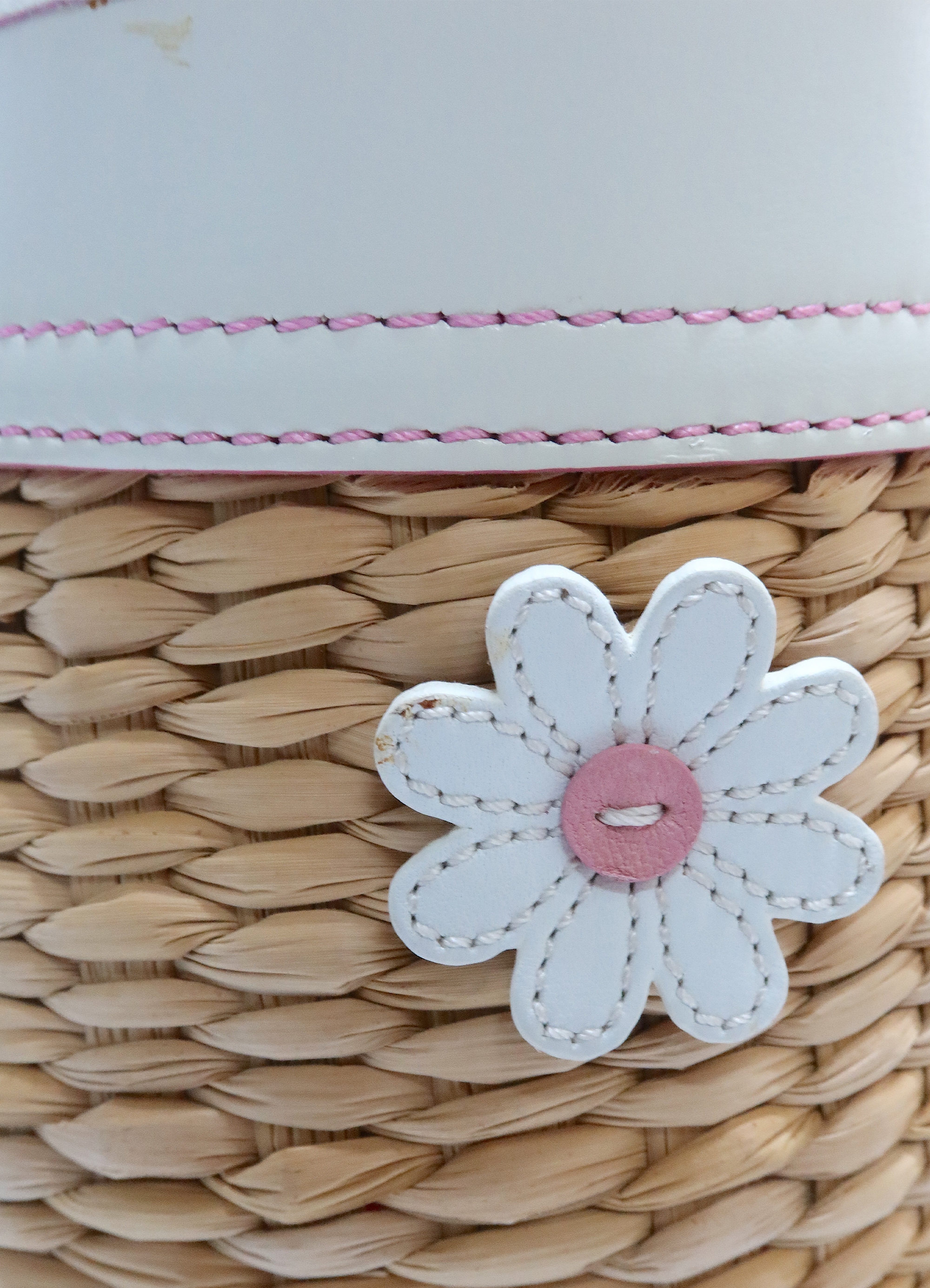 Close up of white leather daisy appliqué with pink center on straw background