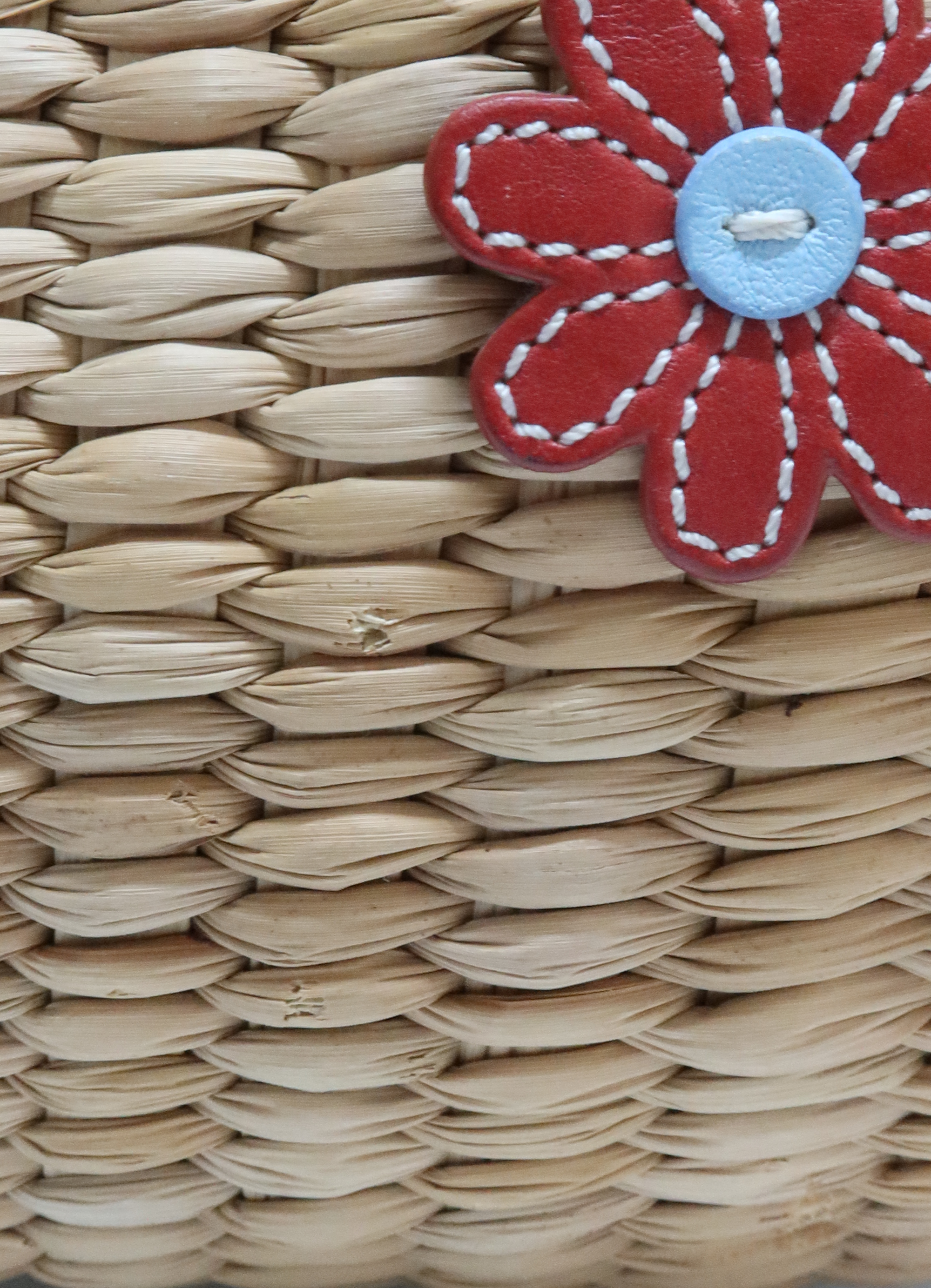 Macro shot of red leather floral appliqué with button center on woven straw